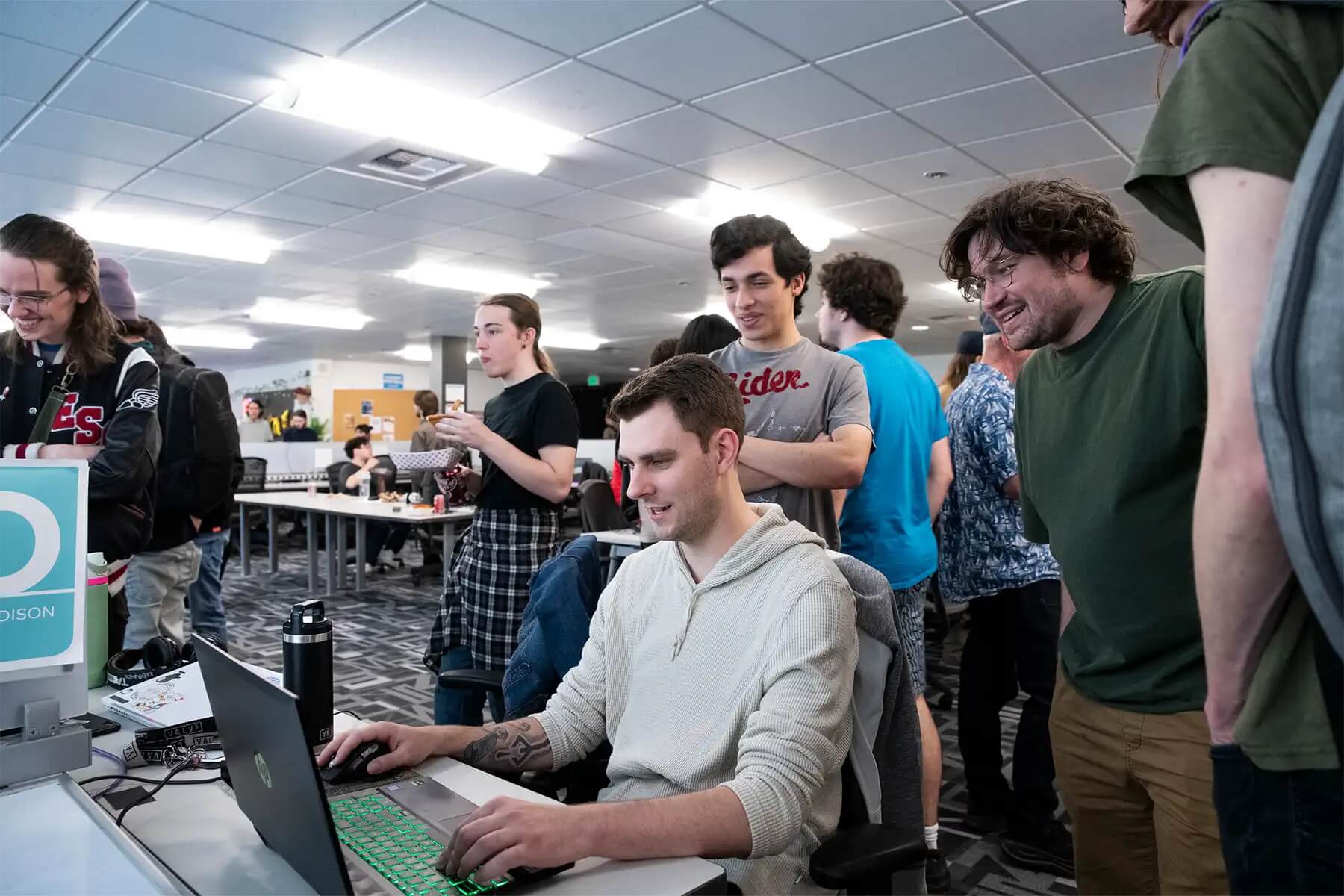 Photo of several college students all smiling, gathered around watching one student working at a laptop. Links to the DigiPen website