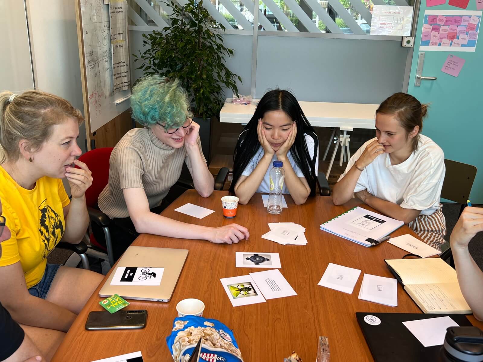 Me (a white woman with green hair) at a table with my coworkers discussing playing card designs