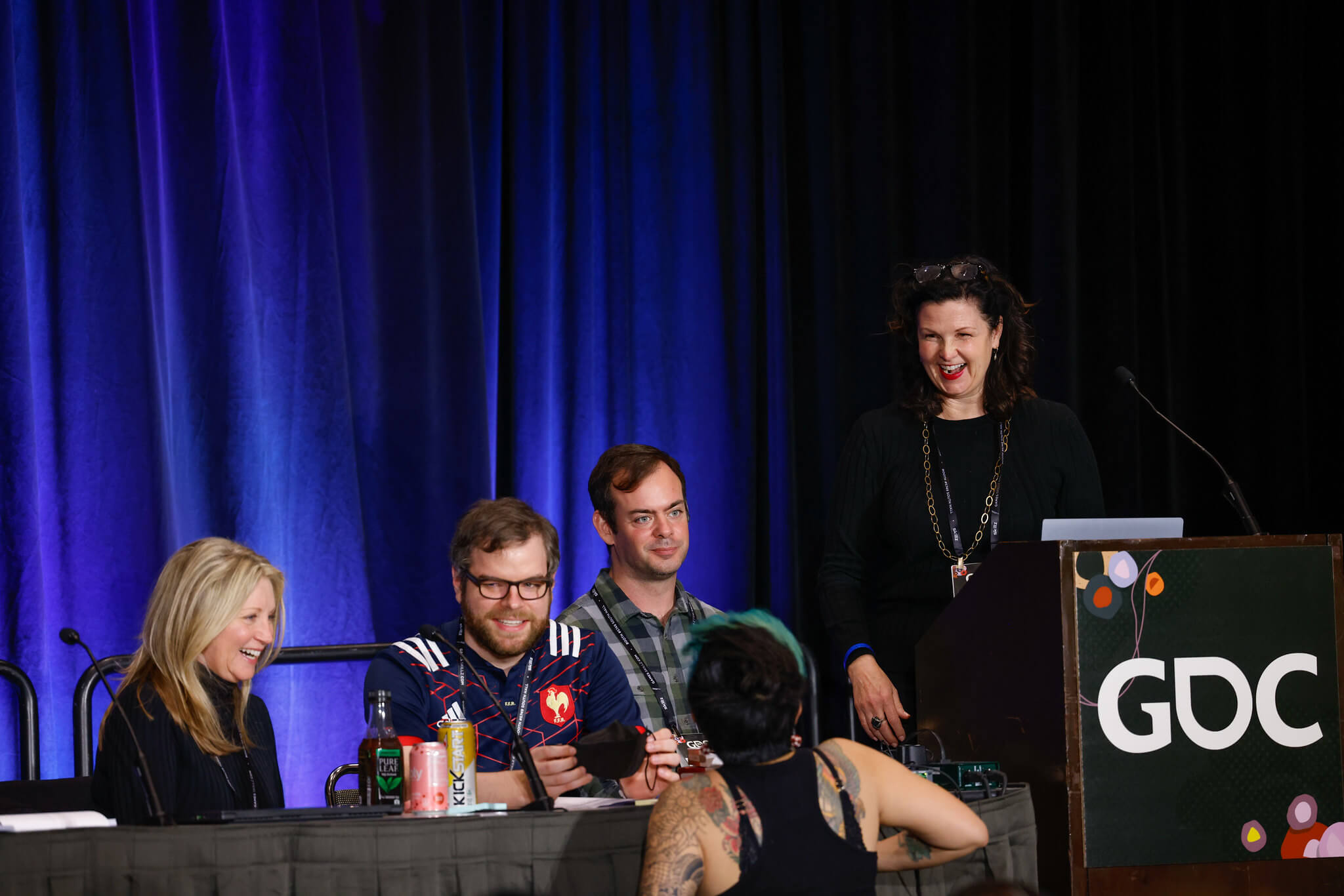 Photo of game developers and members of the Resilience Center sitting at a presenter's table and podium, smiling and discussing during the workshop
